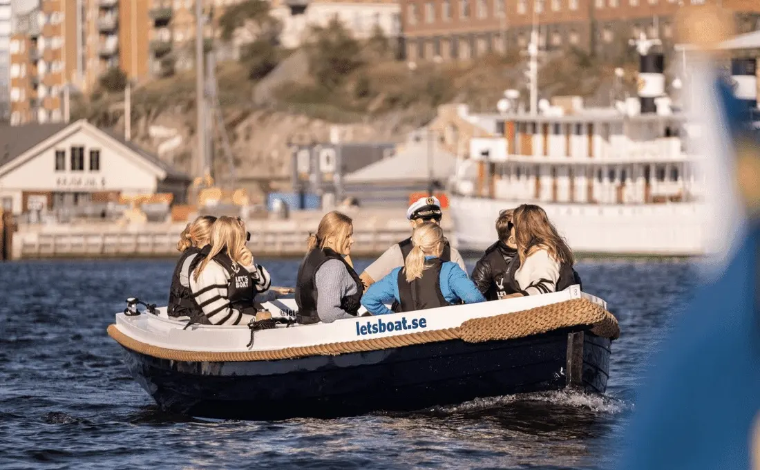Sällskap ombord på en Let's Boat-elbåt med Göteborgs kaj och en vit skärgårdsbåt i bakgrunden.