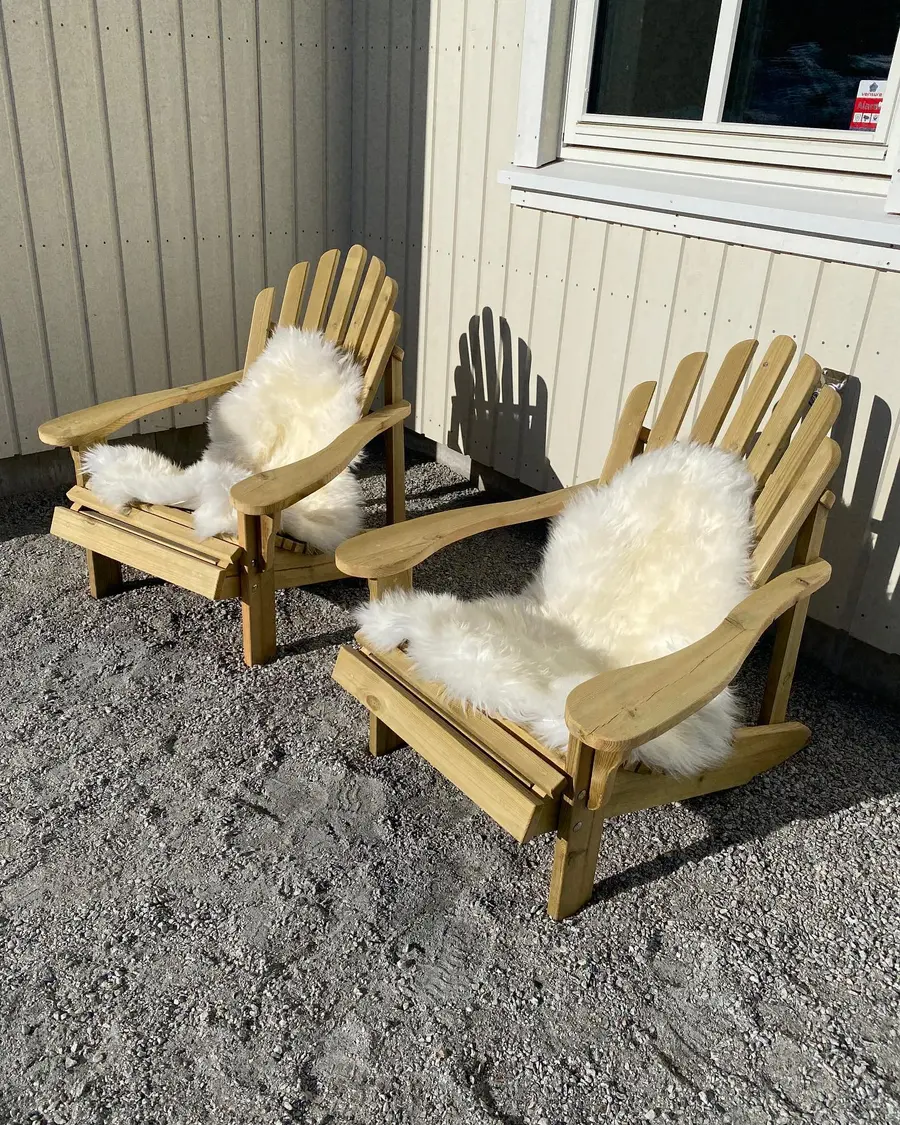 To håndbygde utestoler i tre med saueskinn, montert inntil en husvegg.