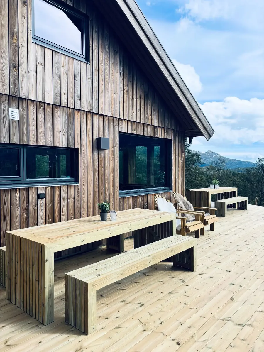 Spesialbygd utebord med benker i tre inntil et trekledd hus.