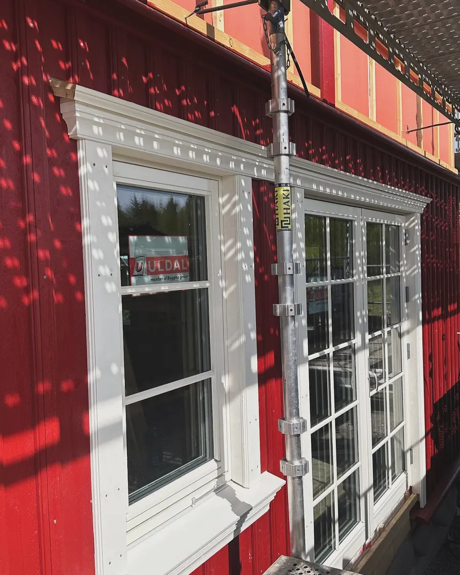 Hvite vindusrammer og lister montert på et rødt trehus.