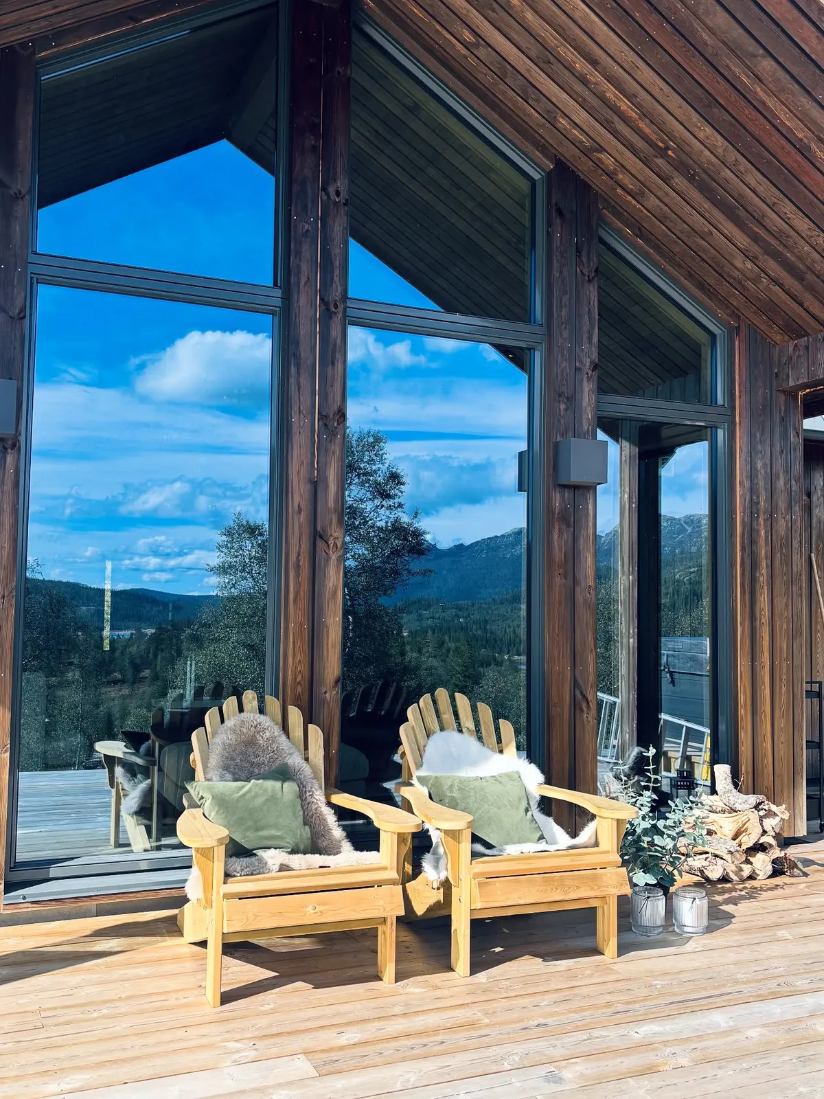 To håndbygde utestoler i tre på en terrasse med vidt utsyn over skog og himmel.